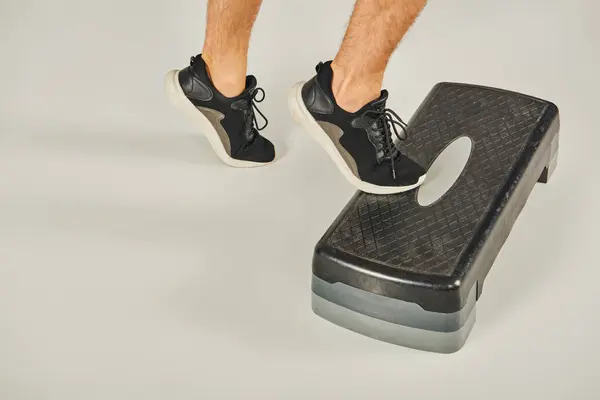 A man in active wear stands confidently atop a step stool against a grey studio background. — Stock Photo