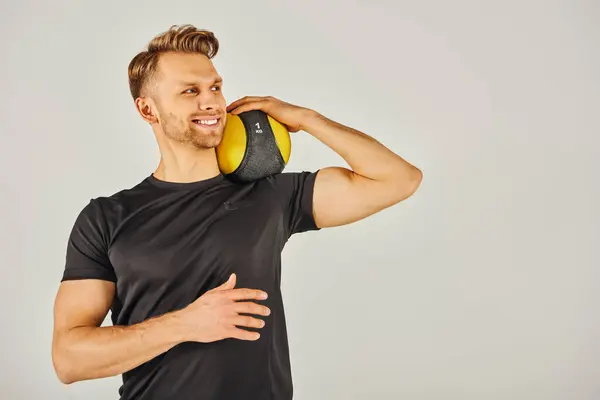 Um jovem desportista em uso ativo segurando uma bola amarela, mostrando equilíbrio e foco em um estúdio com um fundo cinza. — Fotografia de Stock