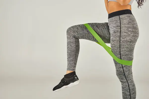 A sportswoman with curly hair wears green band leggings while working out in a studio with a grey background. — Stock Photo