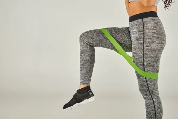 Una sportiva con i capelli ricci indossa leggings a fascia verde mentre lavora in uno studio con uno sfondo grigio. — Foto stock