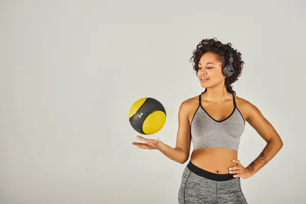 Desportista afro-americano encaracolado em desgaste ativo mostra força e equilíbrio como ela detém uma bola amarela e preta vibrante. — Fotografia de Stock