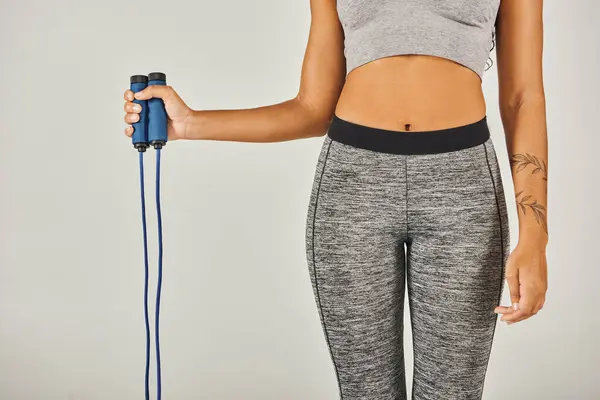 African American sportswoman in active wear energetically holding a jump rope in a studio with a grey background. — Stock Photo