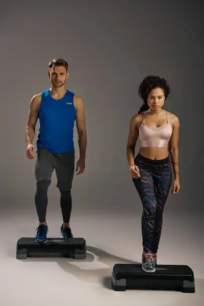 Multicultural, fit couple in active wear balancing on steppers in studio workout session. — Stock Photo