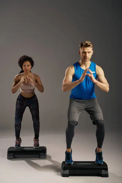 Multicultural, fit couple in active wear working out on steppers in a studio setting. — Stock Photo