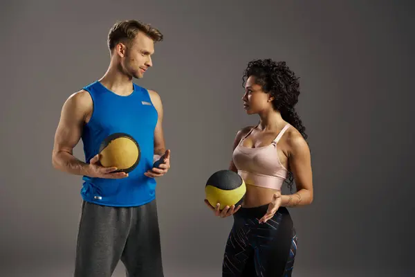 Jovem casal multicultural e apto em desgaste ativo de pé ao lado uns dos outros, segurando bolas de exercício em um ambiente de estúdio. — Fotografia de Stock