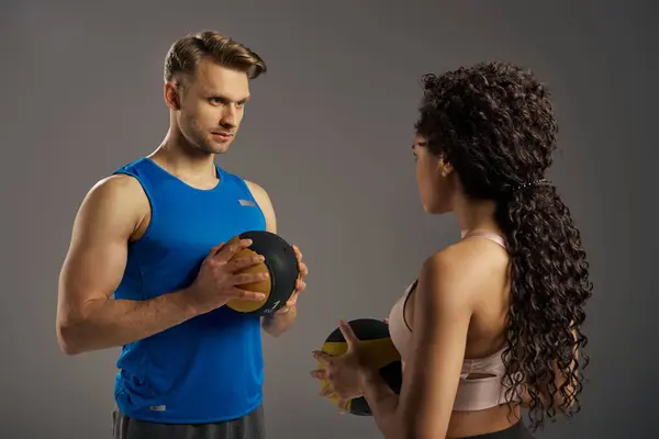 A multicultural couple in active wear grips a weighted ball, showcasing strength and determination in a studio setting. — Stock Photo
