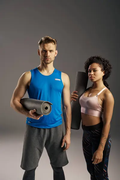 Young multicultural couple in active wear posing with yoga mat in a studio setting. — Stock Photo