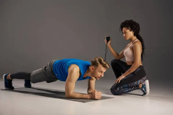 Joven hombre y mujer multicultural en ropa activa haciendo flexiones en una plancha en un estudio, mostrando fuerza y trabajo en equipo. - foto de stock
