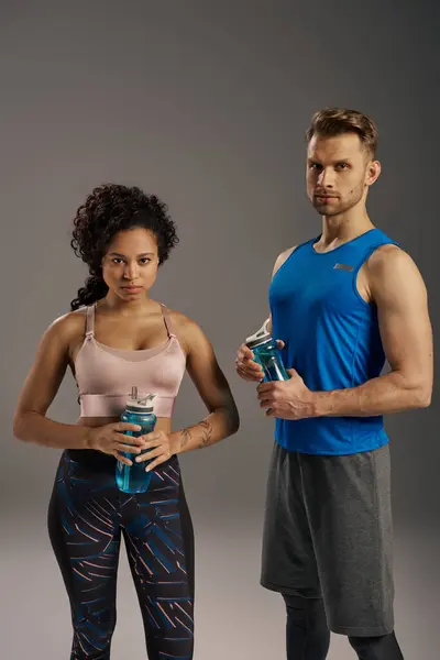 A young multicultural couple in active wear posing gracefully for a portrait on a grey studio background. — Stock Photo