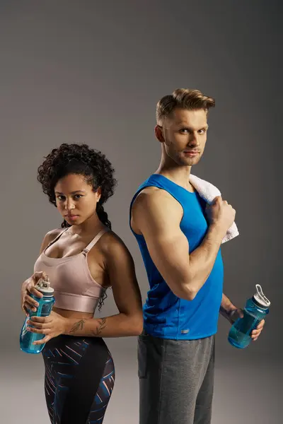 Ein junges multikulturelles und fittes Paar in aktiver Kleidung posiert vor grauem Hintergrund in einem Studio. — Stockfoto