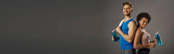 A young multicultural and fit couple in active wear posing confidently in front of a gray background in a studio. — Stock Photo