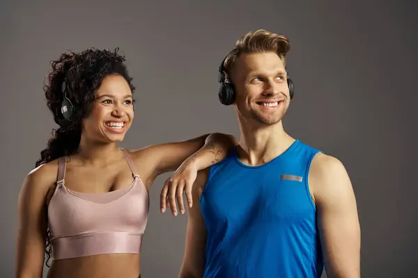 A young multicultural and fit couple, dressed in active wear, are striking a pose for a photo while wearing headphones. — Stock Photo
