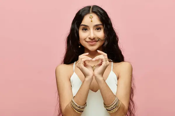 Indian woman forming heart symbol with hands on vibrant pink background. — Stock Photo