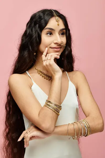 Femme indienne captivante aux cheveux longs pose avec des bijoux en or sur fond rose. — Photo de stock