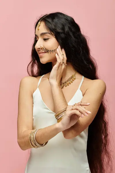 Femme indienne élégante aux cheveux longs et bijoux en or frappant une pose sur fond rose. — Photo de stock
