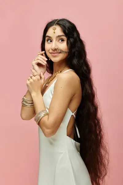 Graceful indian woman with long hair posing elegantly in white dress on pink backdrop. — Stock Photo