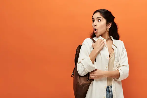 Young indian woman with backpack stands against vivid orange background. — Stock Photo