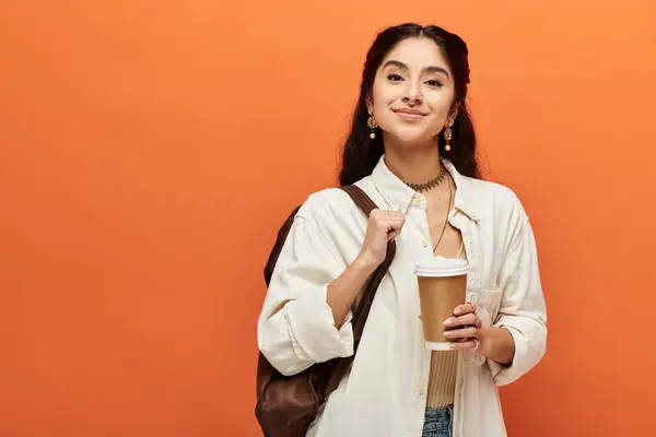 Junge Indianerin genießt eine Tasse Kaffee vor orangefarbenem Hintergrund. — Stockfoto