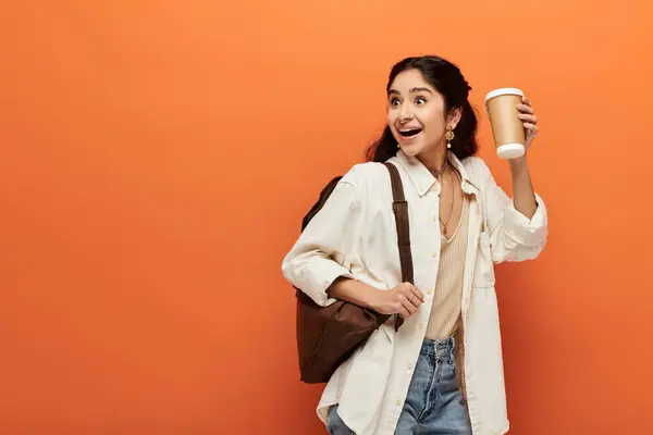 Young indian woman energetically holding coffee against orange backdrop. — Stock Photo