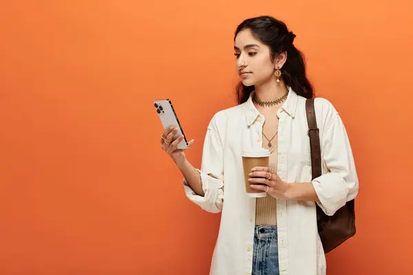 Una giovane donna indiana tiene una tazza di caffè mentre guarda il suo schermo del telefono. — Foto stock