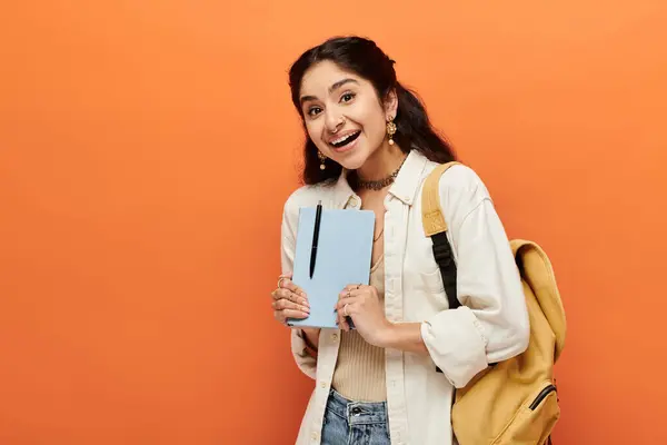 Young indian woman confidently holds notebook on orange background. — Stock Photo