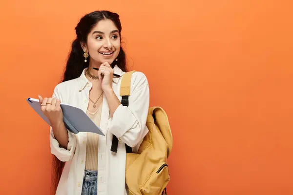 Young indian woman holding a notebook in front of an orange wall. — Stock Photo
