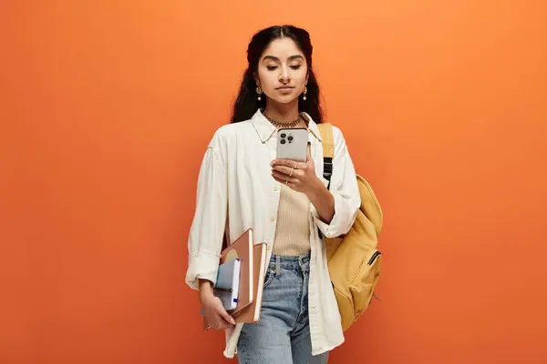 Young indian woman holding a backpack, looking at her phone. — Stock Photo