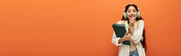 Eine indische Frau hält ein Buch vor orangefarbenem Hintergrund. — Stockfoto