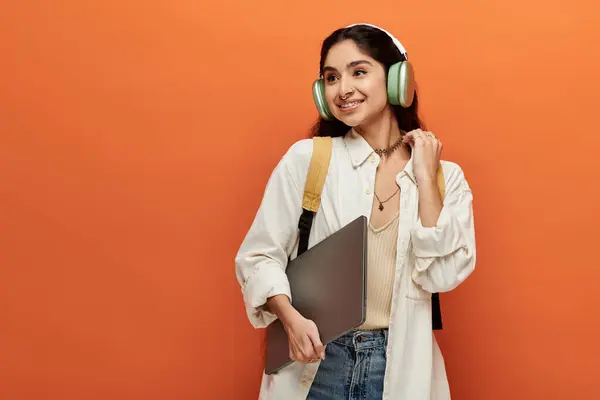 Young indian woman with headphones, holding laptop on orange background. — Stock Photo