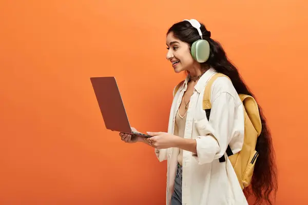 Young indian woman with headphones using laptop on vibrant orange background. — Stock Photo