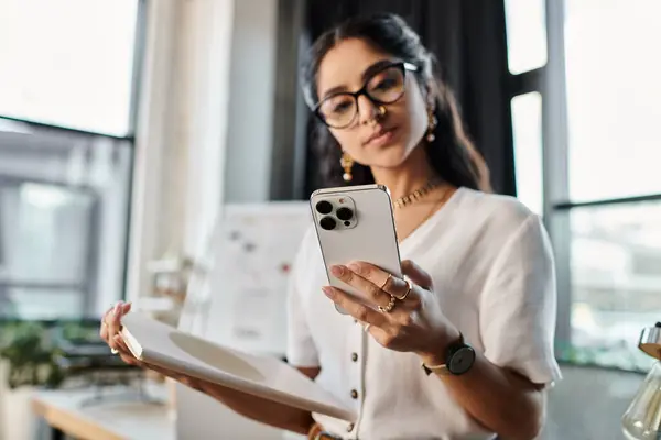 Stylish indian woman with glasses holding phone, focused on screen. — Stock Photo