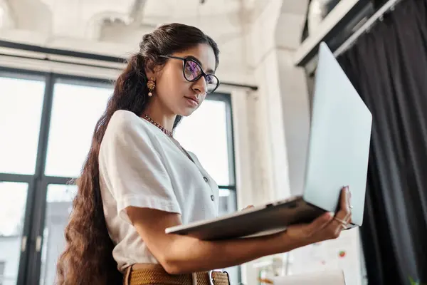 Attractive indian woman with glasses using laptop in office. — Stock Photo