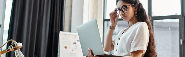 A indian woman in glasses is using a laptop in an office. — Stock Photo