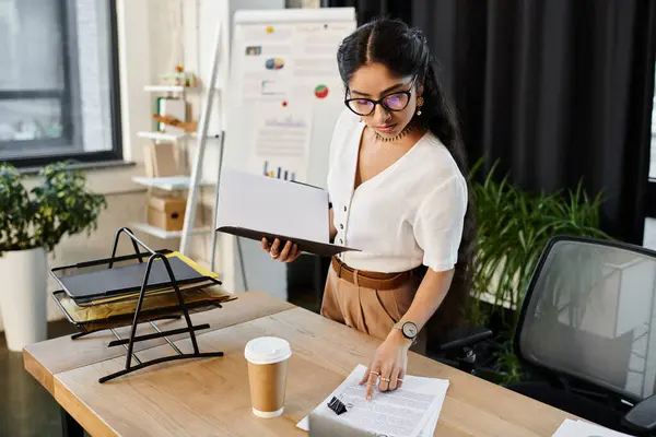 Young indian woman in glasses, standing at desk with laptop. — Stock Photo