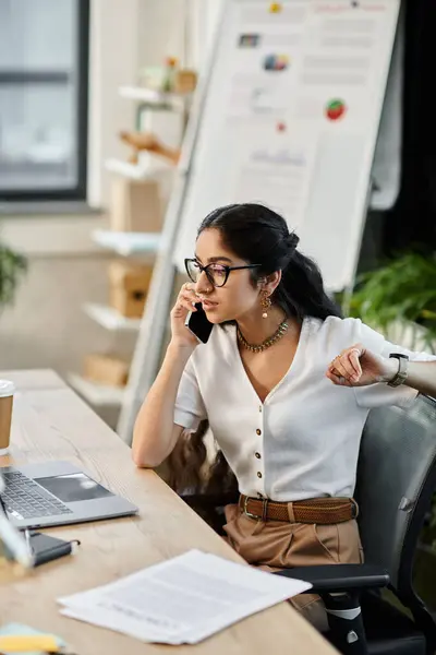 Mujer india joven hablando por teléfono mientras está sentada en el escritorio. - foto de stock