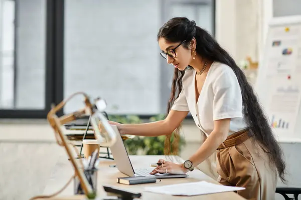 Uma jovem mulher indiana trabalhando ativamente em um laptop em um ambiente de escritório. — Fotografia de Stock