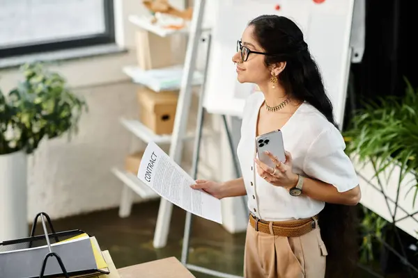 Una donna indiana che sembra determinata mentre sta in piedi accanto a una scrivania con una carta in mano. — Foto stock