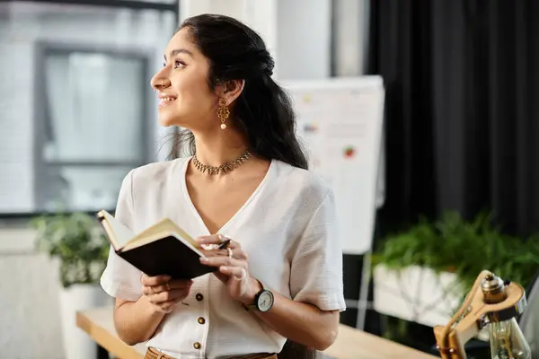 Young indian woman engrossed in reading a book in a modern office setting. — Stock Photo