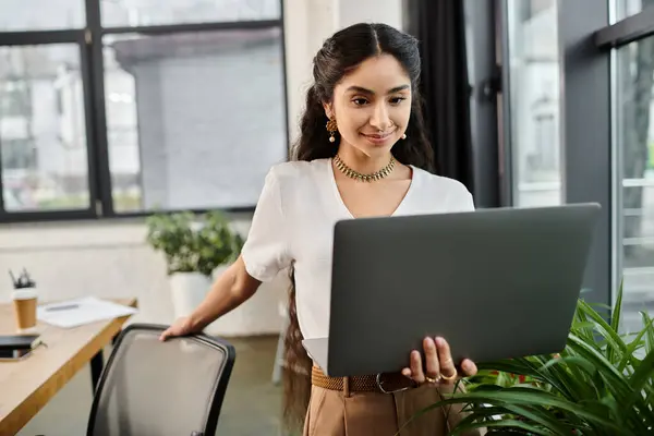 Una giovane donna indiana concentrata che lavora meticolosamente sul suo portatile in un ufficio moderno. — Foto stock