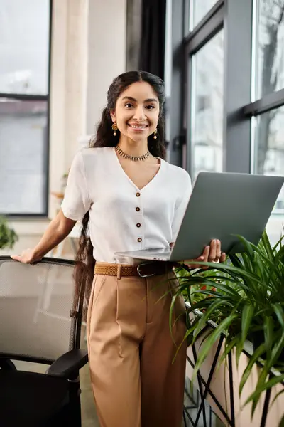 Young indian woman with laptop standing by plant. — Stock Photo