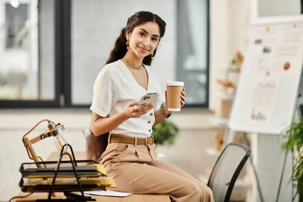 Eine junge Indianerin sitzt an einem Schreibtisch und hält elegant eine Tasse Kaffee. — Stockfoto