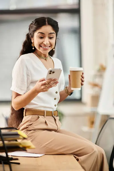 Indian woman with coffee and phone at desk. — Stock Photo