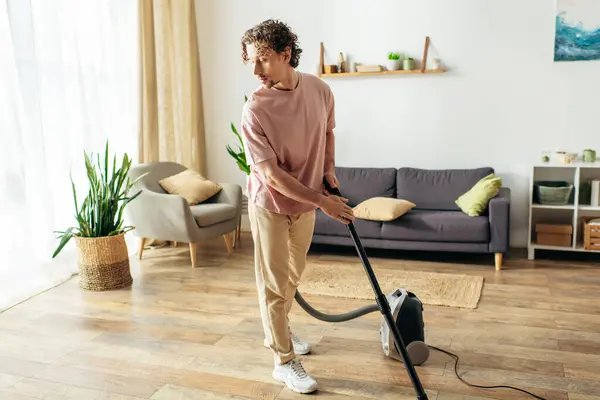 Um homem bonito em roupa de casa acolhedora usa um vácuo para limpar sua sala de estar. — Fotografia de Stock