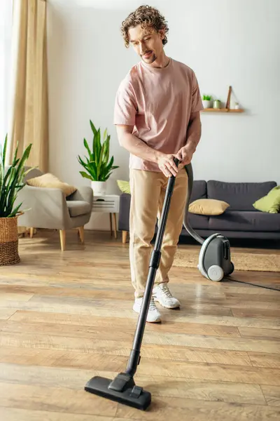 Schöner Mann in kuscheliger Homewear reinigt gekonnt den Boden mit einem Staubsauger. — Stockfoto