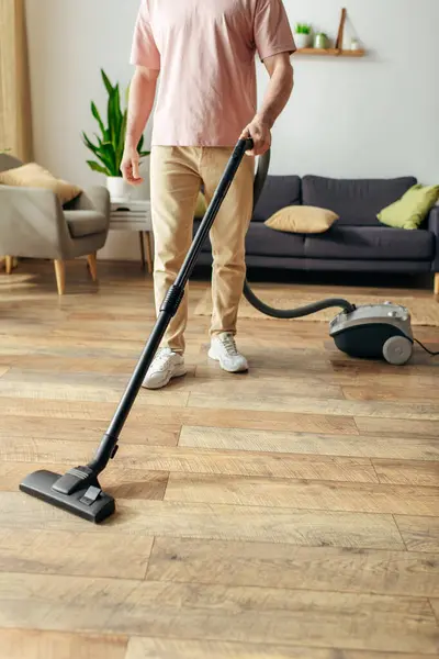 A man in cozy homewear uses a vacuum to clean a wooden floor. — Stock Photo