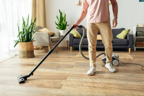 A handsome man in cozy homewear using a vacuum to clean the floor. — Stock Photo