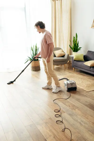 Ein gutaussehender Mann in kuscheliger Hauskleidung reinigt den Boden mit einem Staubsauger. — Stockfoto