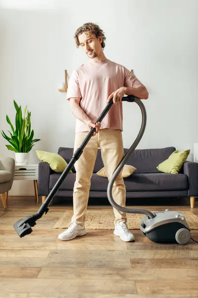 Красивий чоловік у затишному домашньому вбранні використовує вакуум для чищення підлоги. — стокове фото
