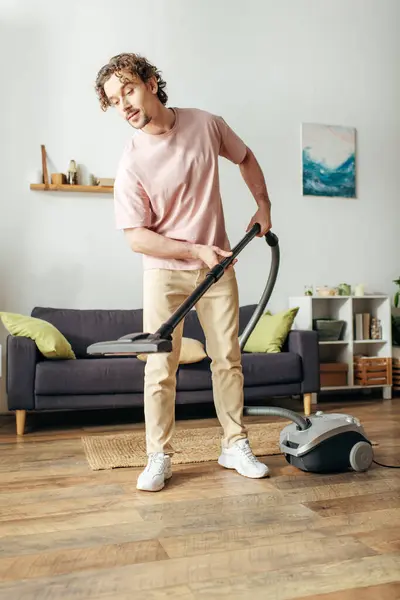 A handsome man in cozy homewear diligently vacuums his living room. — Stock Photo