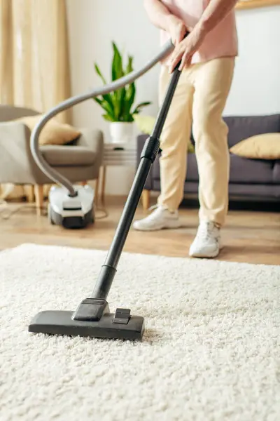 A handsome man in cozy homewear diligently vacuums a carpet with a vacuum cleaner. — Stock Photo